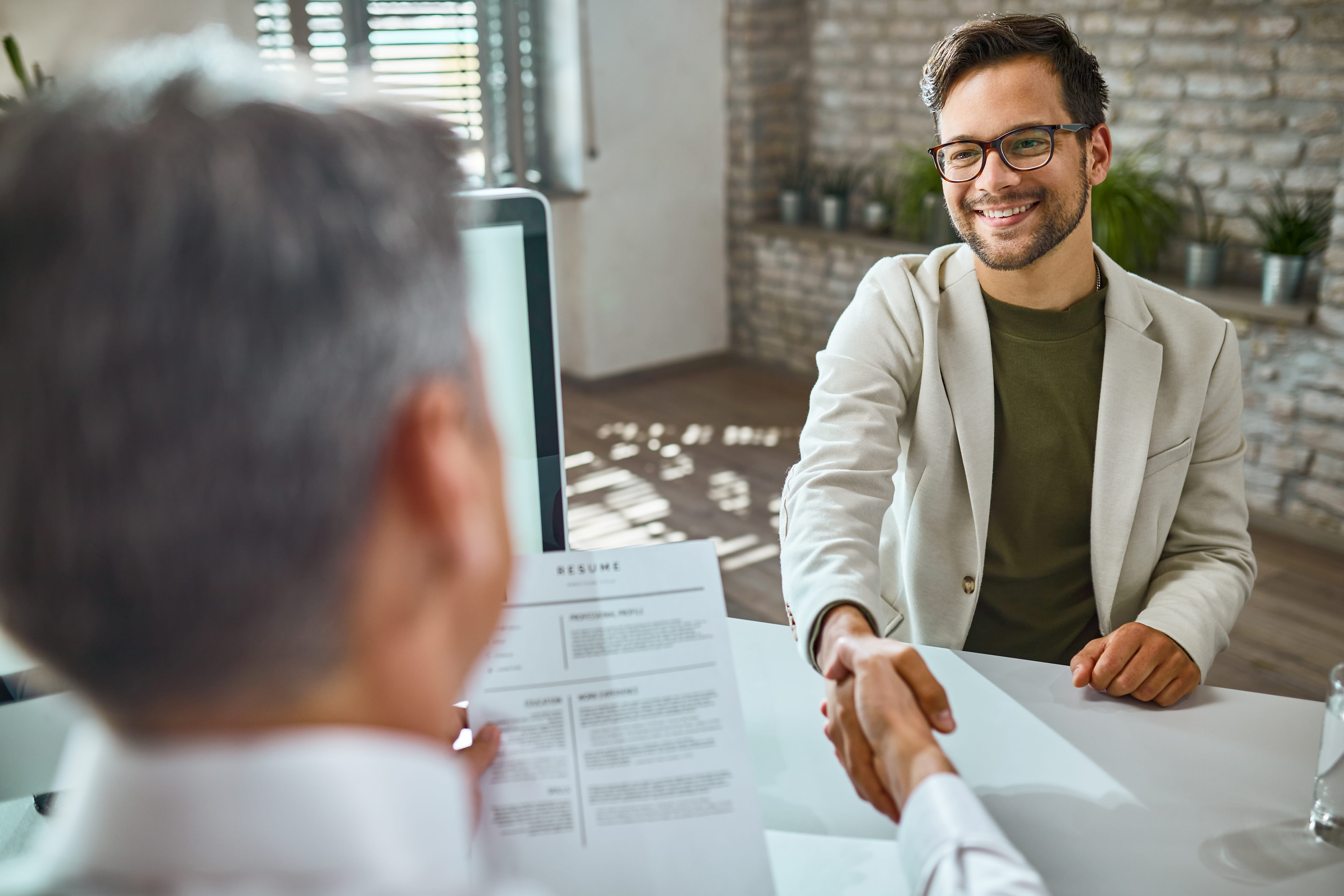 candidato masculino feliz cumprimentando membro da equipe de recursos humanos em entrevista de emprego no escritório